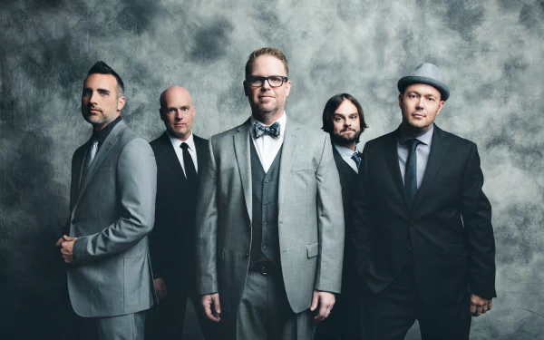 HD desktop wallpaper featuring a group of five men in stylish suits standing against a textured grey background, tagged with 'mercyme'.