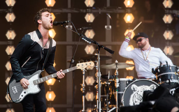A dynamic performance by Royal Blood, showcasing the band’s energetic style, with a bassist singing passionately and a drummer intensively playing in a vibrant stage setting.