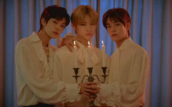 Three members of ENHYPEN pose together, holding a candelabrum, dressed in elegant white shirts, against a softly lit backdrop. A striking HD wallpaper celebrating music and artistry.