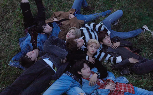 A high-definition desktop wallpaper featuring the members of ENHYPEN, lying together on grass in casual attire, creating a relaxed and youthful atmosphere.