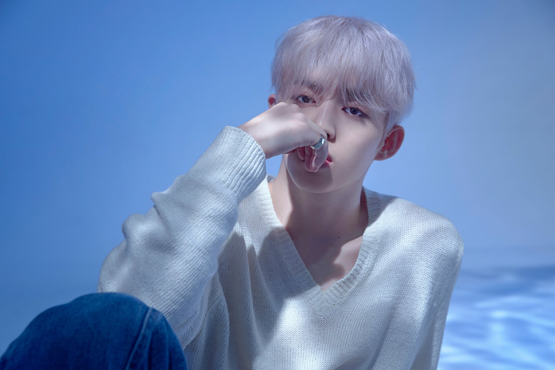 A serene HD desktop wallpaper featuring a member of Seventeen, captured in soft lighting, wearing a cozy sweater and looking contemplatively at the camera.