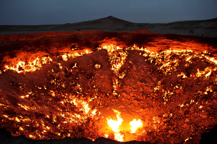 HD desktop wallpaper showing the Darvaza Gas Crater in Turkmenistan, with glowing flames illuminating the desert night landscape.