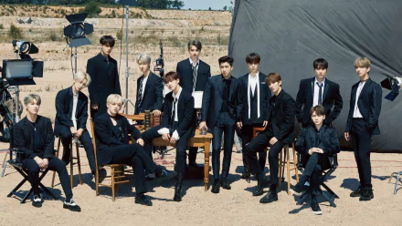Group of thirteen stylish individuals posing for a high-definition desktop wallpaper with the tag Seventeen, featuring an outdoor photoshoot setup in a sandy location.