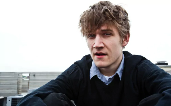 HD desktop wallpaper featuring a thoughtful man with tousled hair in casual attire against a blurred outdoor backdrop.