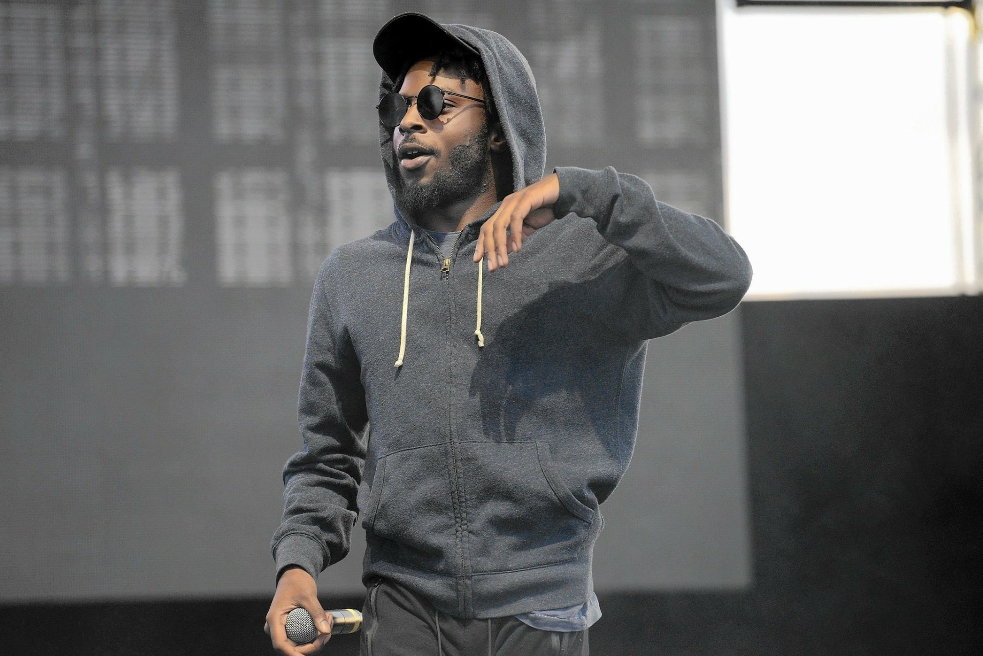 HD desktop wallpaper featuring a man in a hoodie performing on stage, representing Isaiah Rashad.