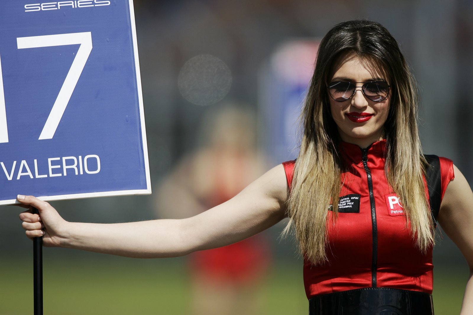 HD PC desktop wallpaper and background of a cute grid girl model in a red outfit holding a trackside sign at a motorsport event.