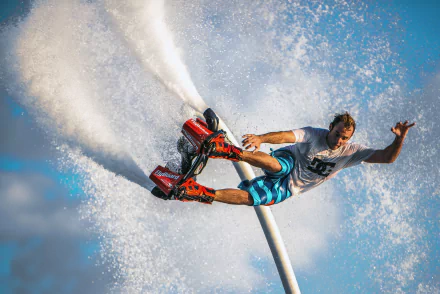 HD wallpaper of a person performing extreme flyboarding tricks with water jets against a blue sky background.