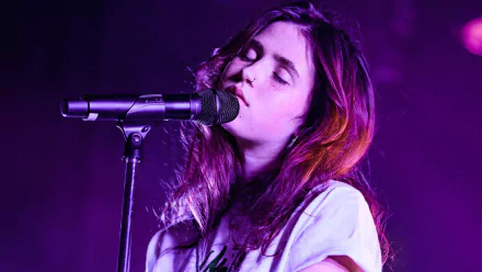 HD desktop wallpaper of a female musician performing at a microphone with purple stage lighting.