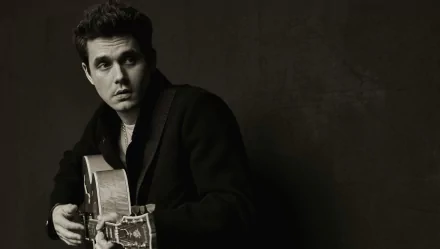 A monochrome HD desktop wallpaper featuring a man holding a guitar against a textured backdrop.