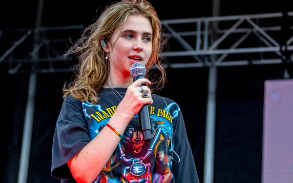 HD desktop wallpaper featuring Clairo on stage with a microphone, wearing a graphic t-shirt.