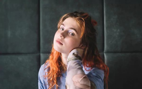 HD desktop wallpaper featuring a contemplative person with auburn hair against a dark tufted background, embodying a pensive and artistic vibe.