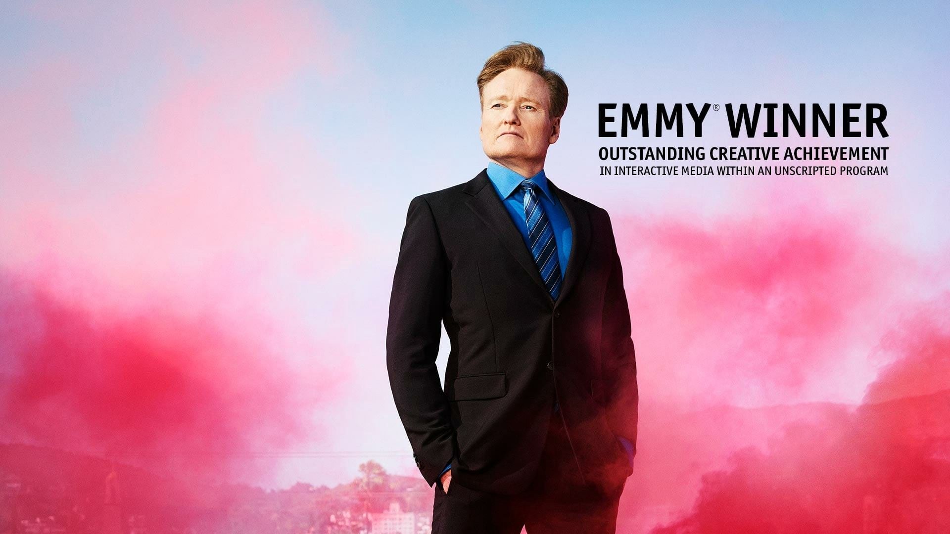 HD desktop wallpaper featuring a man standing confidently with EMMY WINNER text, against a vibrant pink smoke background.
