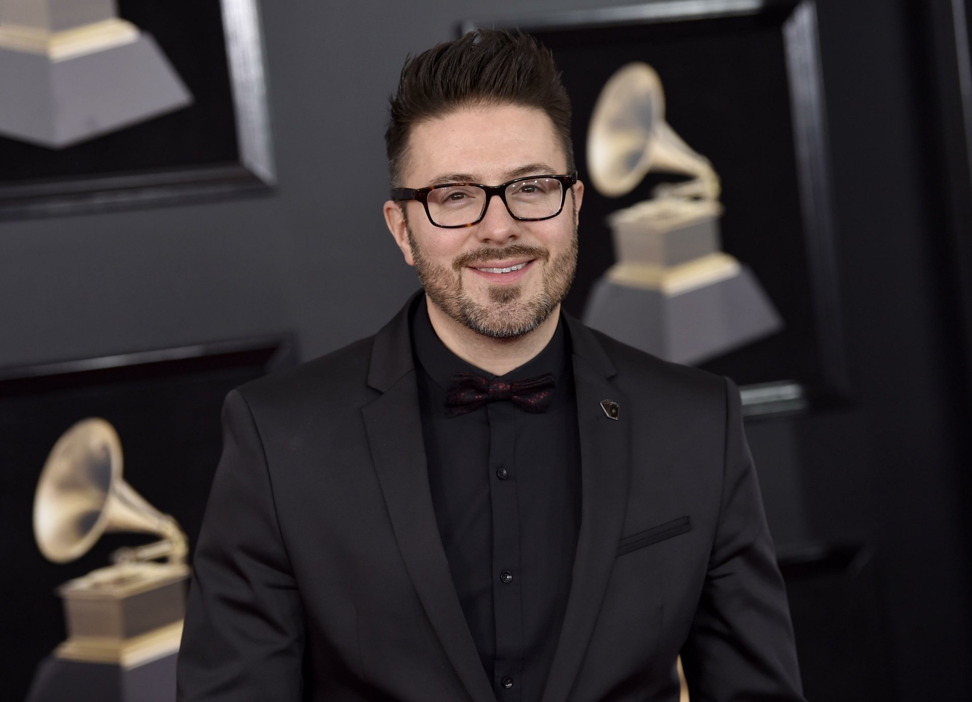 A man in a black suit and glasses posing at an event with Grammy Awards in the background, as an HD desktop wallpaper.