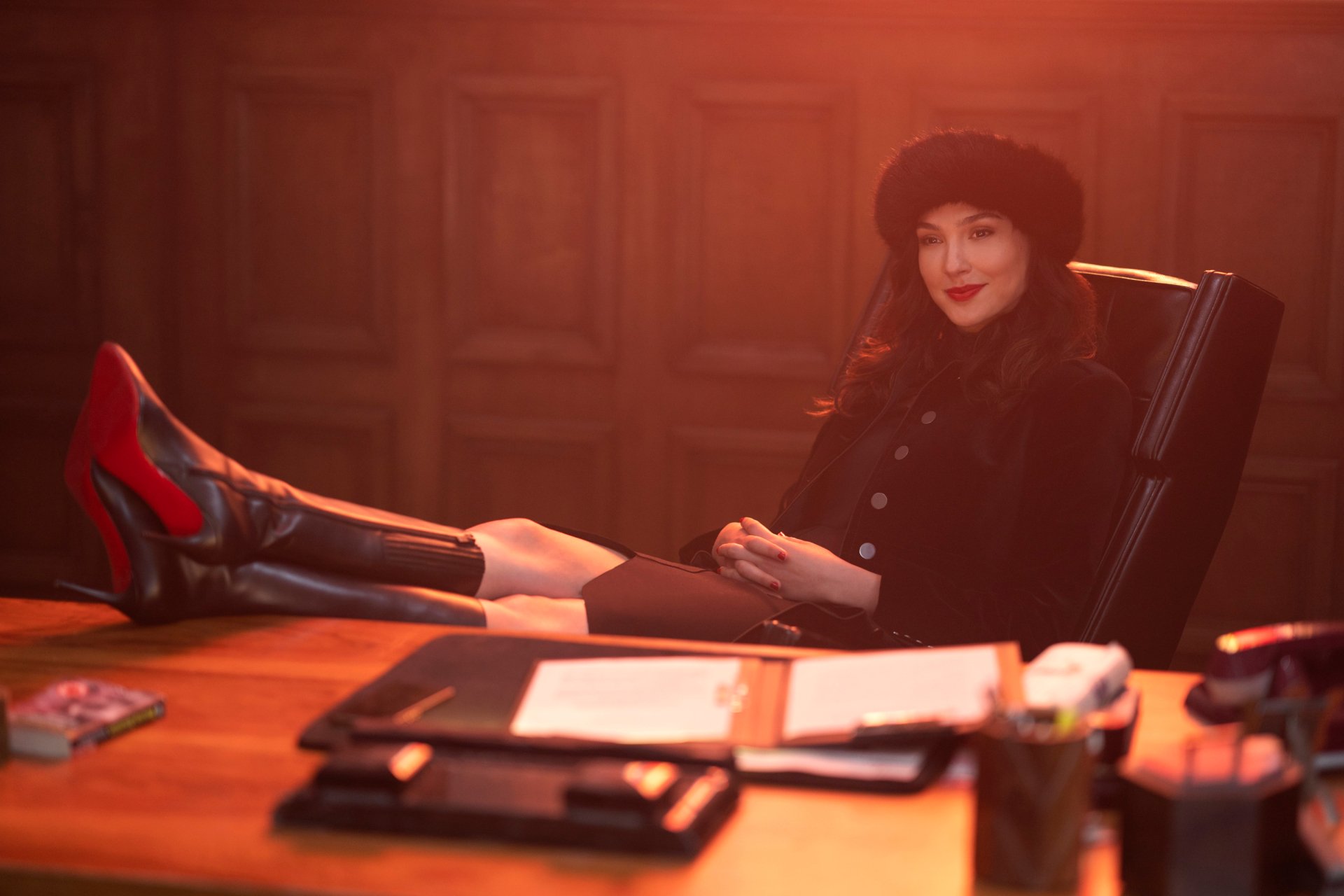 2K Quad HD desktop wallpaper: woman in fur hat and coat lounges with red heels on a desk in a wood-paneled office, cinematic lighting referencing the movie Red Notice.