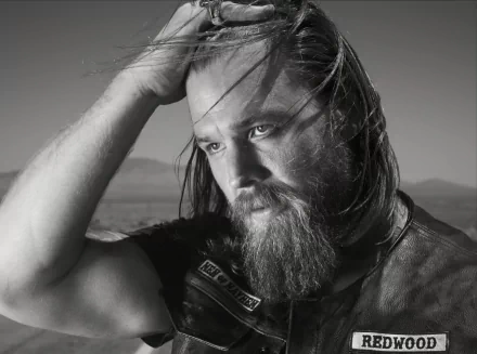 Black and white HD wallpaper featuring a bearded man in a leather vest, reminiscent of a Sons of Anarchy character, posing against a blurred natural backdrop.