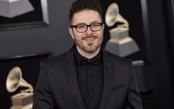A man in a black suit and glasses posing at an event with Grammy Awards in the background, as an HD desktop wallpaper.