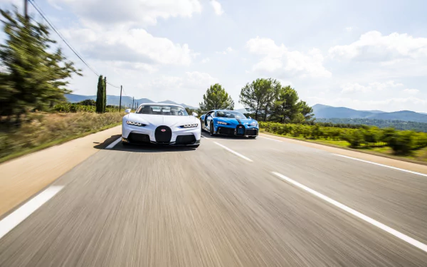 Two Bugatti Chiron supercars speeding down a sunlit open road — 8K Ultra HD PC desktop wallpaper background of high-performance vehicles.
