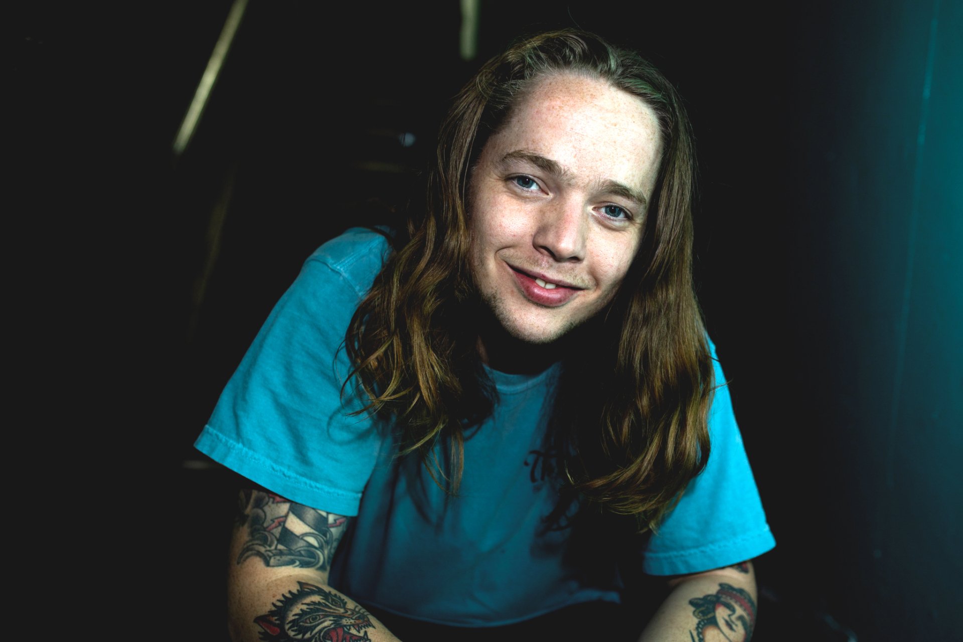 HD wallpaper featuring a smiling person with long hair and tattoos, suitable as a desktop background.