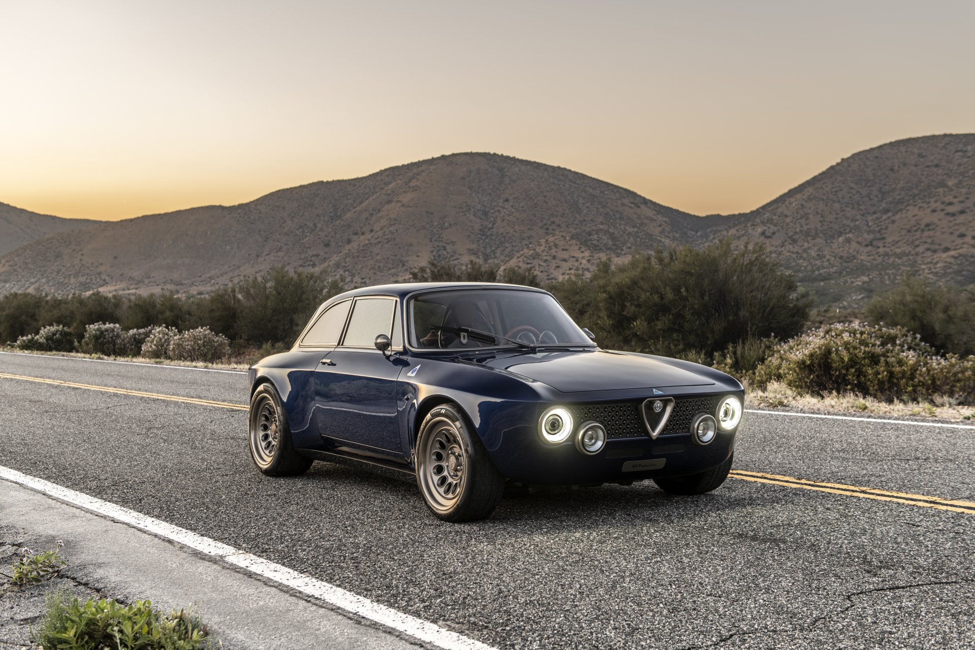 8K Ultra HD PC desktop wallpaper of a Totem Automobili GT Electric — navy electric car parked on a scenic highway at sunset with rolling hills.