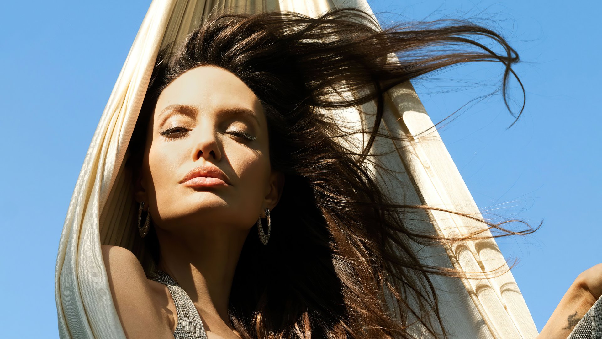 4K Ultra HD desktop wallpaper featuring a close-up of celebrity Angelina Jolie with flowing hair against a clear blue sky background.