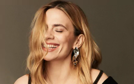 HD PC desktop wallpaper of a smiling blonde female celebrity with shoulder-length hair partially covering one eye, wearing statement earrings and a black top.