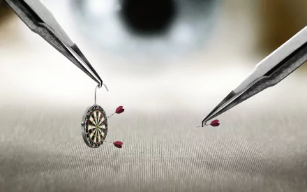 HD desktop wallpaper featuring a man-made miniature dartboard being held by tweezers with tiny darts in motion against a blurred background.
