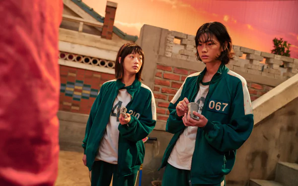 Ji-Yeong and Kang Sae-byeok from the TV show Squid Game stand outdoors in their numbered green tracksuits at sunset, captured in a 4K Ultra HD desktop wallpaper.