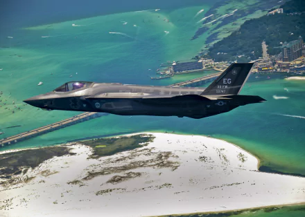 Military Lockheed Martin F-35 Lightning II jet flying over a coastal area, captured in high-definition for a PC desktop wallpaper and background.