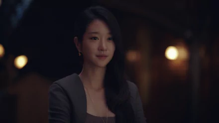 HD PC desktop wallpaper of a poised celebrity woman with long dark hair in a dim, warmly lit room, wearing a dark blazer and subtle earrings.