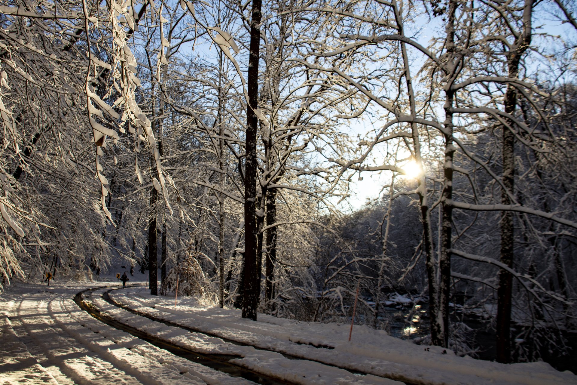 5K Ultra HD PC desktop wallpaper and background: winter sunset over a snow-covered forest and winding road, sun filtering through bare, ice-glazed trees.