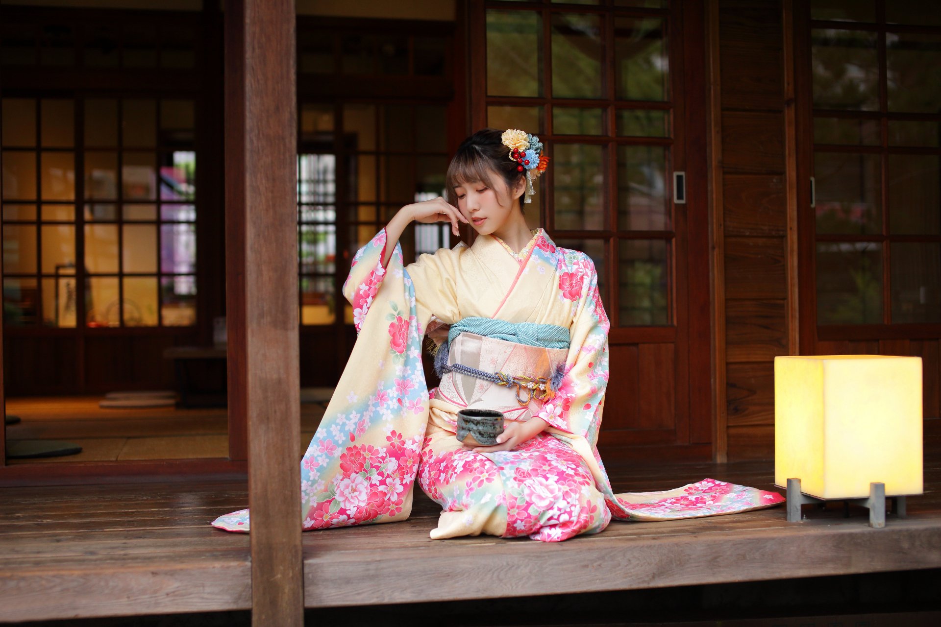 An Asian woman in a floral kimono seated on a wooden porch, captured in stunning 4K Ultra HD for a PC desktop wallpaper and background.