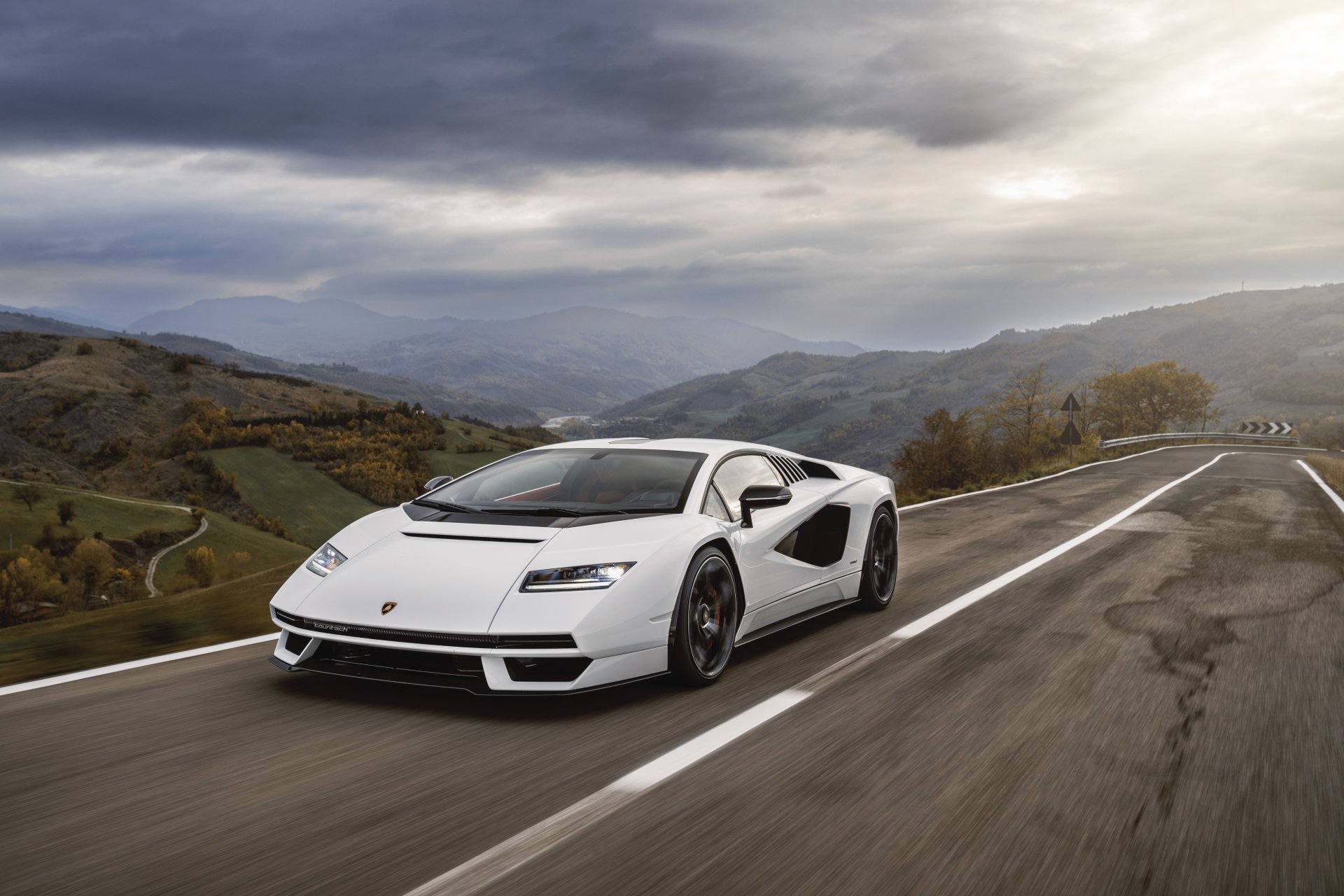 White Lamborghini Countach LPI 800-4 supercar vehicle speeding on a winding mountain road under a dramatic sky — 8K Ultra HD PC desktop wallpaper background.