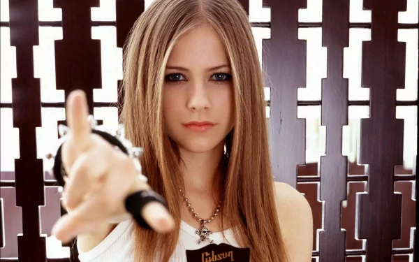 A young woman with long hair points forward confidently, set against a patterned background. This HD wallpaper features Avril Lavigne, embodying a bold music vibe.