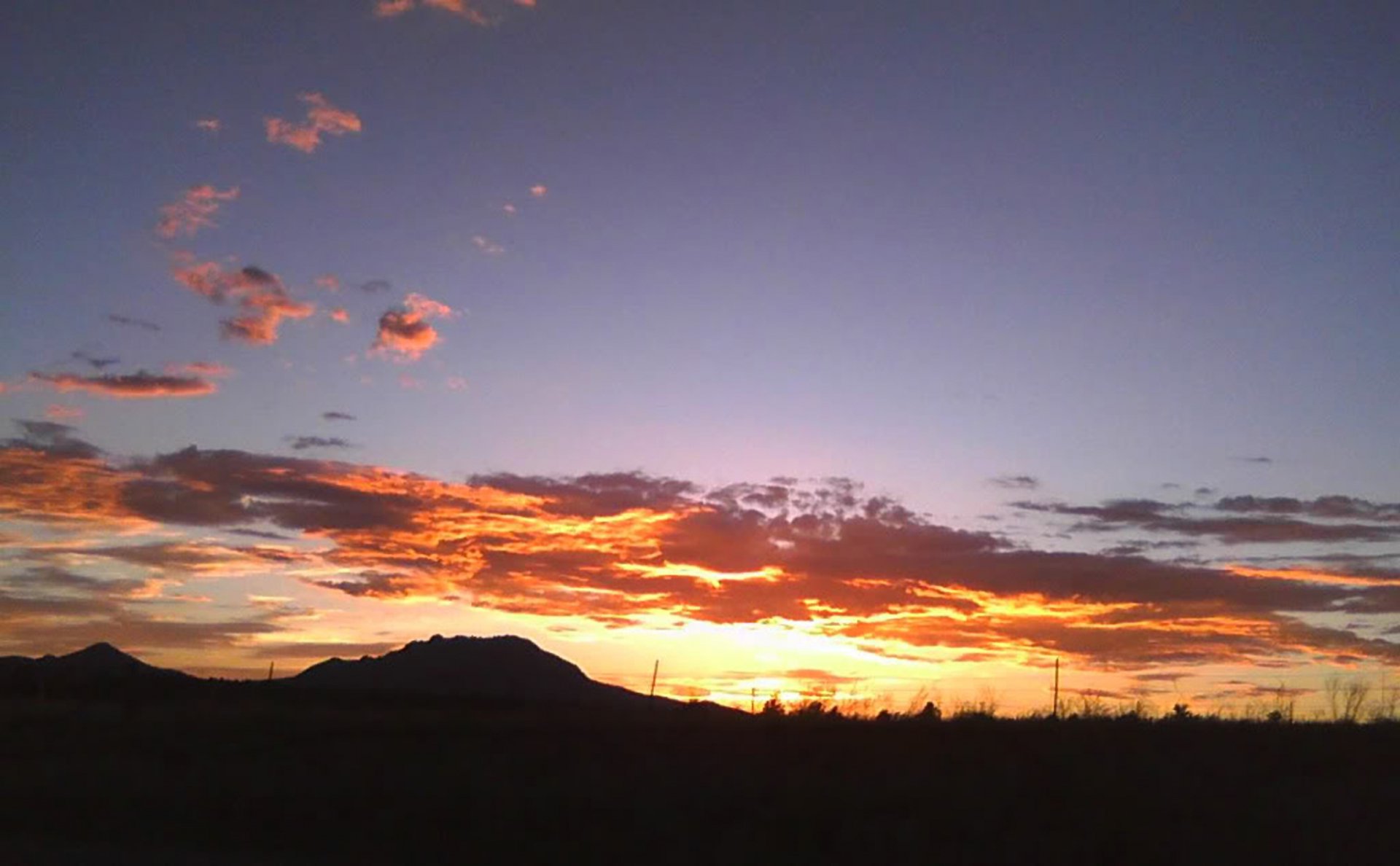 HD PC desktop wallpaper capturing a vibrant desert sunset with fiery clouds against a deepening sky, showcasing nature’s serene beauty.