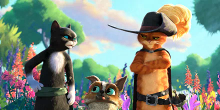 HD PC desktop wallpaper of Puss in Boots (from Puss in Boots: The Last Wish) standing with a black cat and a small dog companion in a vibrant, flowered meadow background.