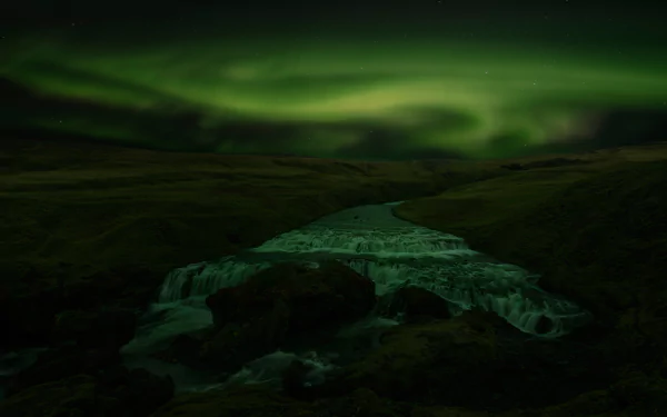8K Ultra HD PC desktop wallpaper/background — night nature scene: vivid green aurora borealis swirling above a dark river and rugged terrain.
