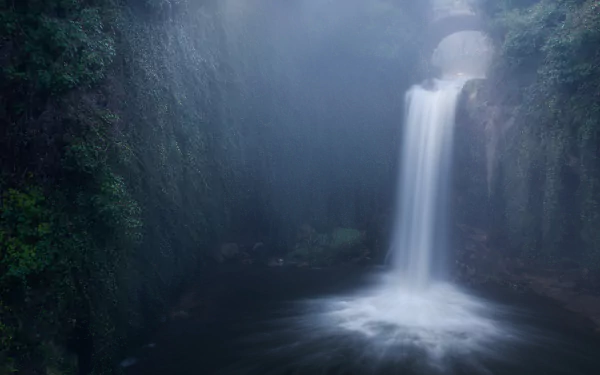 HD desktop wallpaper featuring a serene waterfall cascading into a misty pool, surrounded by lush greenery and rocky cliffs in a tranquil natural setting.