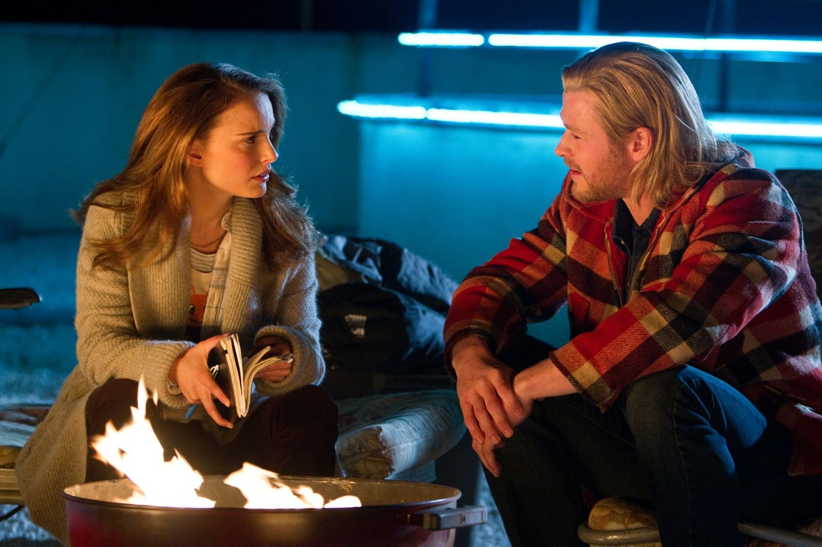 A scene from Thor featuring Natalie Portman as Jane Foster and Chris Hemsworth, sitting by a campfire in a cozy setting, creating a captivating backdrop for any desktop.