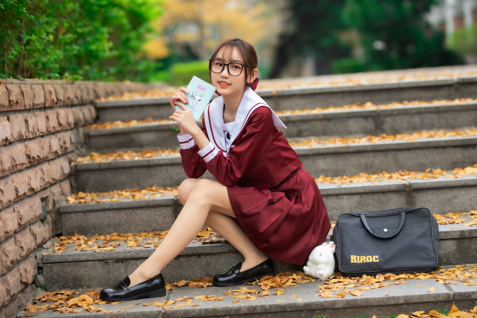 Asian woman in a maroon dress sitting on outdoor steps, holding a phone and wearing glasses. 4K Ultra HD PC desktop wallpaper and background.