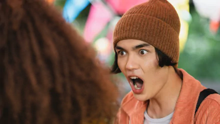 HD PC desktop wallpaper and background of TV show Heartstopper: a wide-eyed teen in a brown beanie yells in surprise against colorful blurred party bunting.