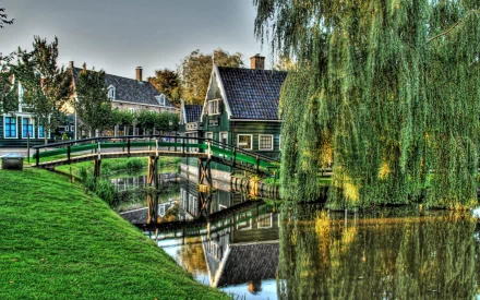 HDR photography captures a serene village scene with a green wooden bridge over calm water, lush trees, and traditional houses, creating an HD desktop wallpaper background.