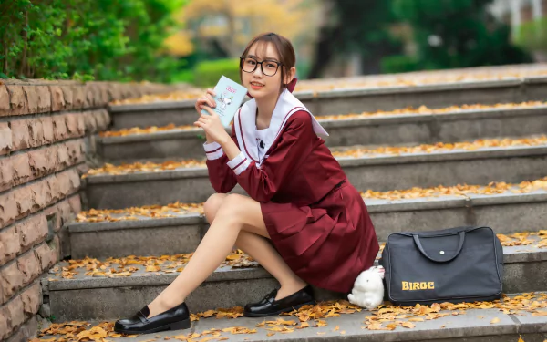 Asian woman in a maroon dress sitting on outdoor steps, holding a phone and wearing glasses. 4K Ultra HD PC desktop wallpaper and background.