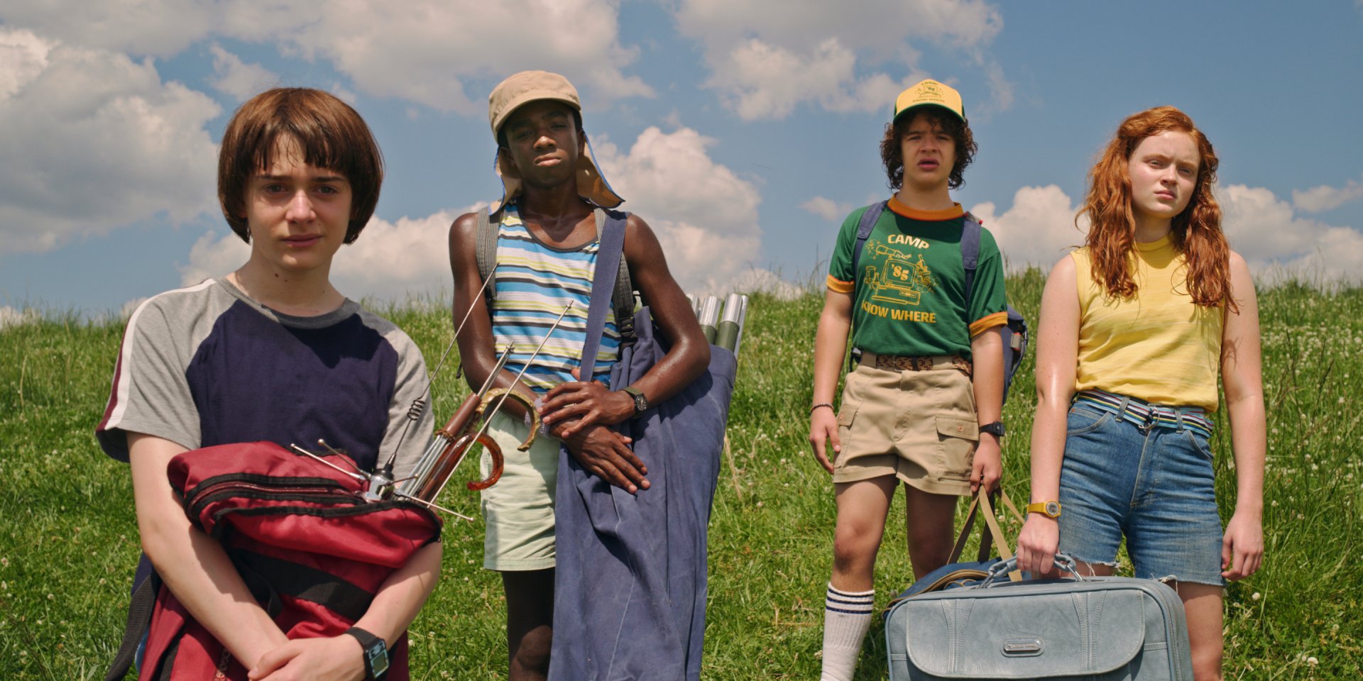 HD PC desktop wallpaper of four teens standing on a grassy hill under a blue sky — Stranger Things TV show–themed background.