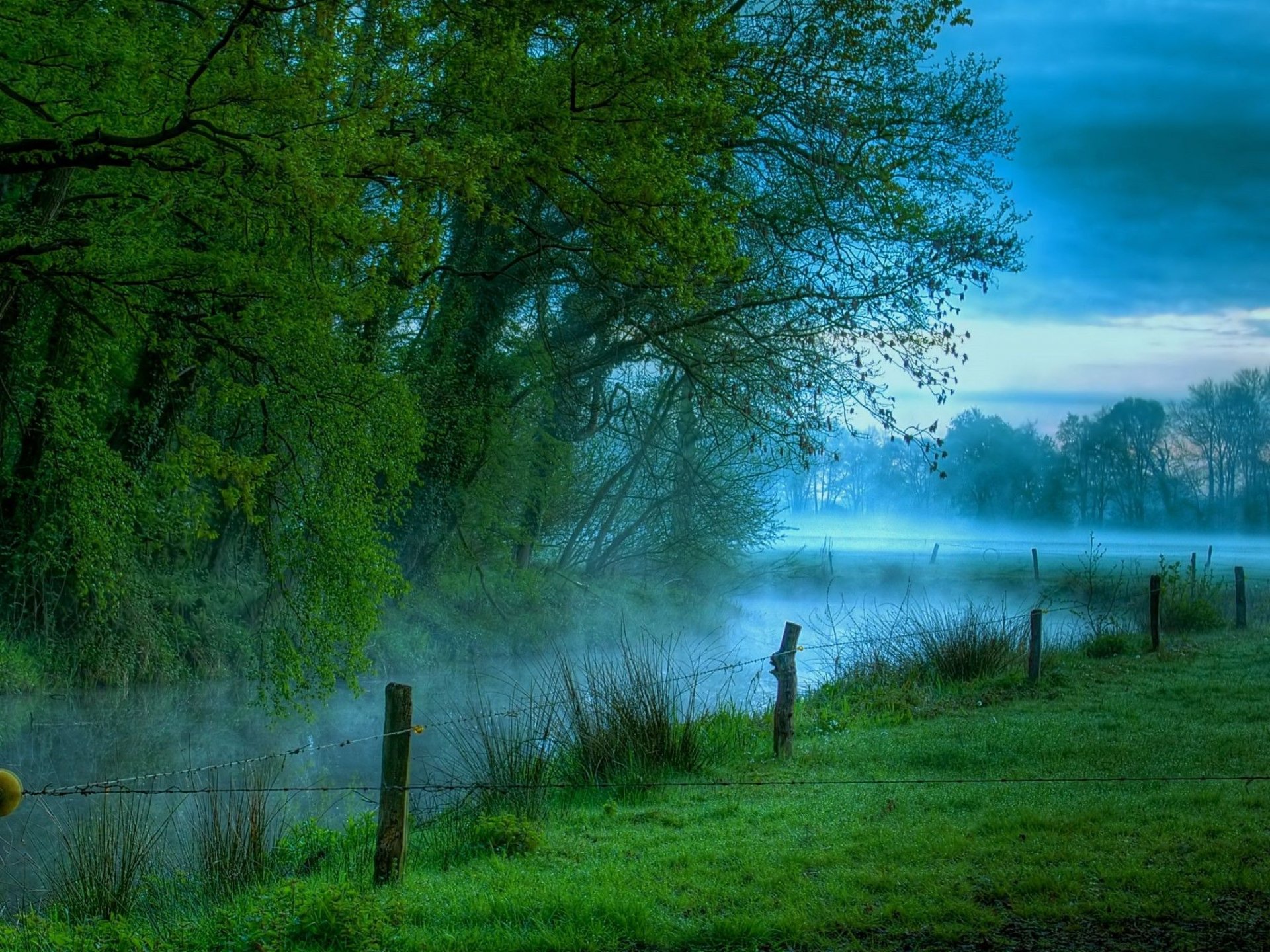 Misty blue-green river winding through trees and a grassy bank with fence posts at dawn — HD PC desktop wallpaper background (nature, river)