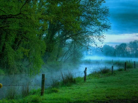 Misty blue-green river winding through trees and a grassy bank with fence posts at dawn — HD PC desktop wallpaper background (nature, river)