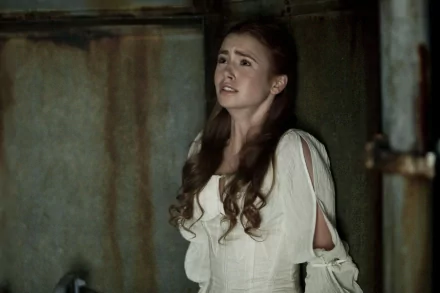 Lily Collins in a tense moment from the movie Priest, dressed in a white gown and conveying vulnerability against a gritty background. HD wallpaper capturing this cinematic scene.