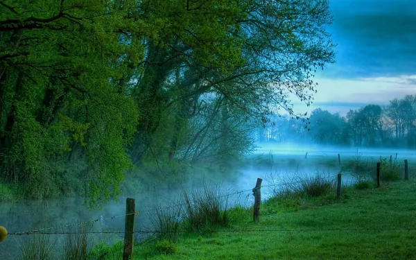 Misty blue-green river winding through trees and a grassy bank with fence posts at dawn — HD PC desktop wallpaper background (nature, river)