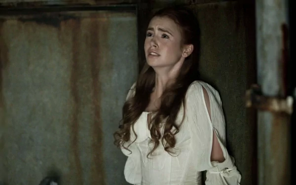 Lily Collins in a tense moment from the movie Priest, dressed in a white gown and conveying vulnerability against a gritty background. HD wallpaper capturing this cinematic scene.