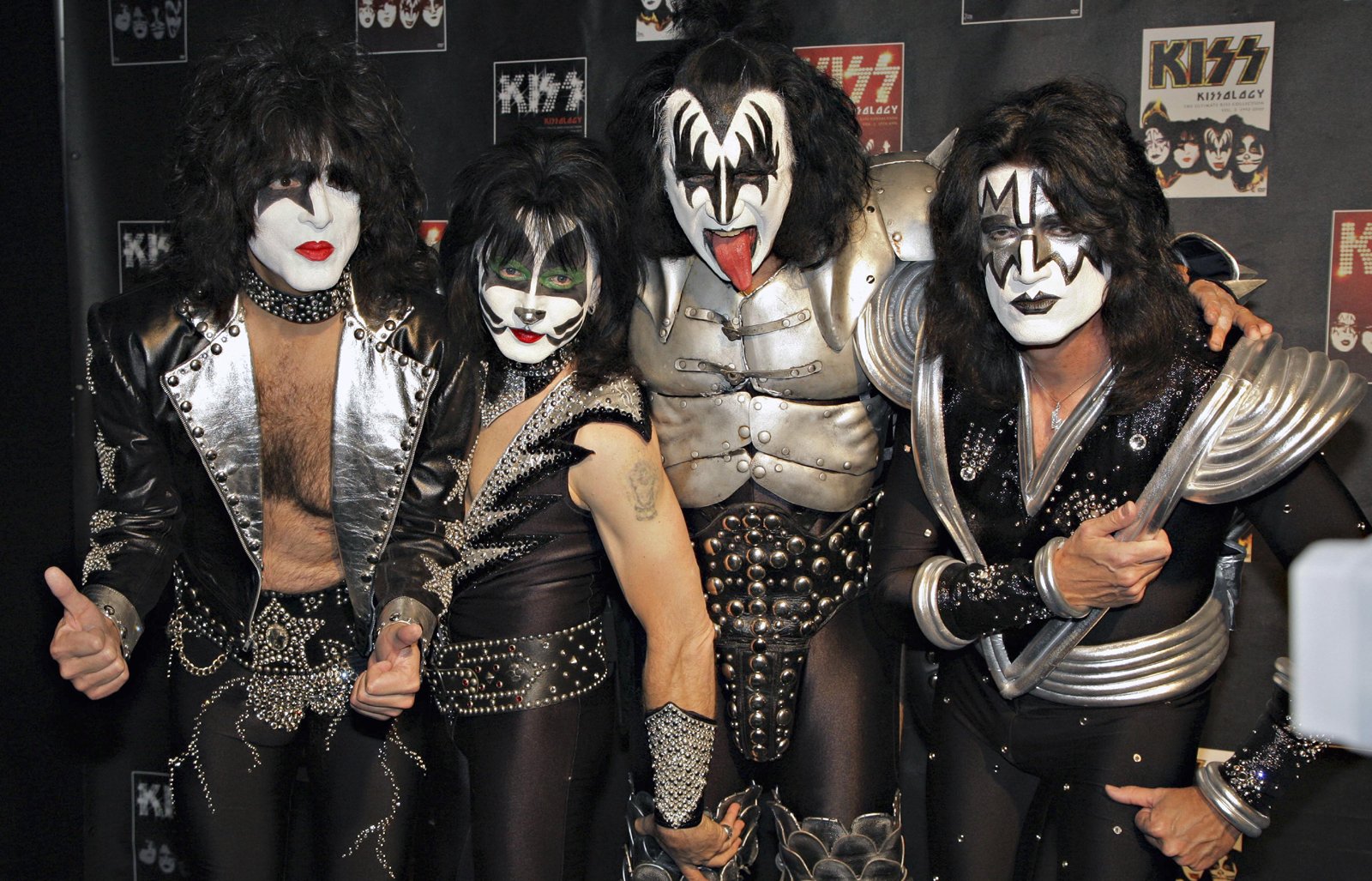 HD music desktop wallpaper of four glam-rock musicians in black-and-white face paint and metallic armor-like stage costumes, dramatic theatrical makeup and posed for a promo shot.