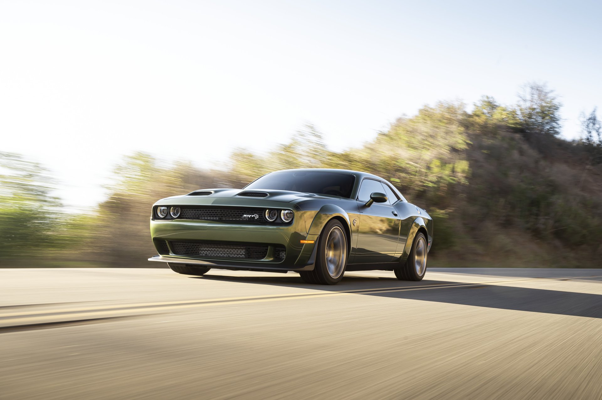 A black Dodge Challenger SRT speeding on a sunlit road with blurred trees in the background, captured in a sharp 4K Ultra HD desktop wallpaper image.